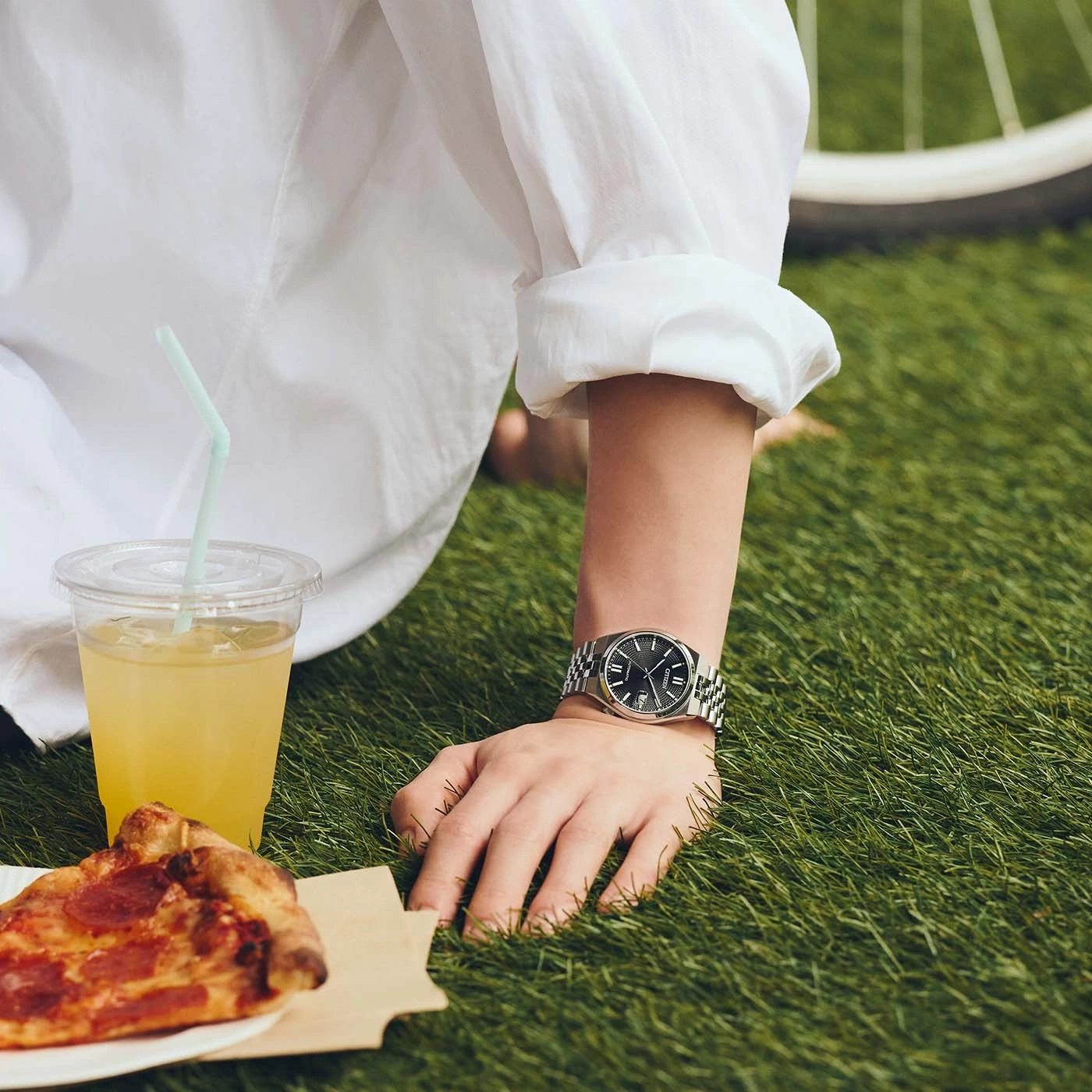 Een persoon in een wit overhemd geniet van een picknick met pizza en een drankje.