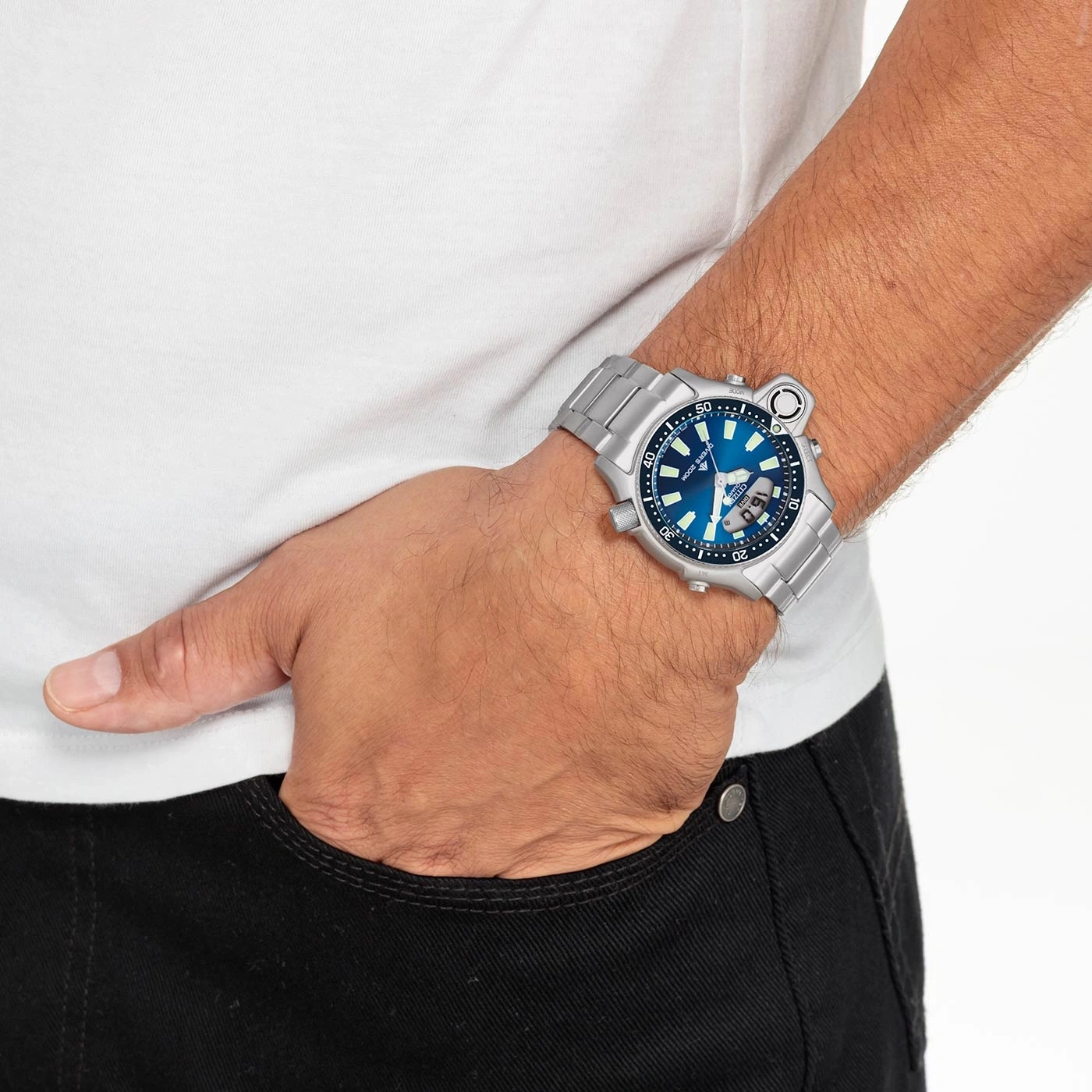 Man draagt zilveren horloge met blauwe wijzerplaat, hand in zak.
