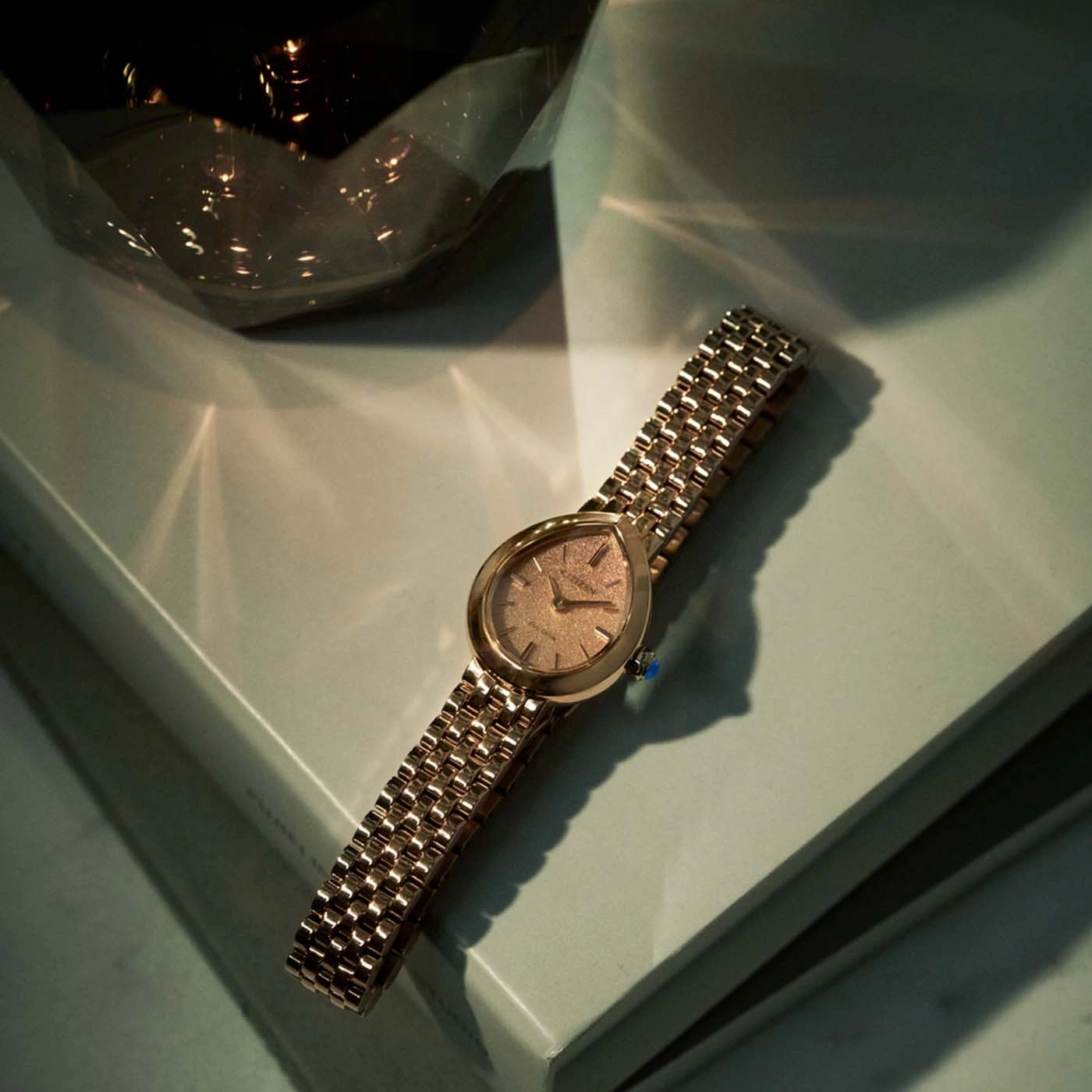 Een gouden horloge met een patroonwijzerplaat ligt op een lichtgroen oppervlak.