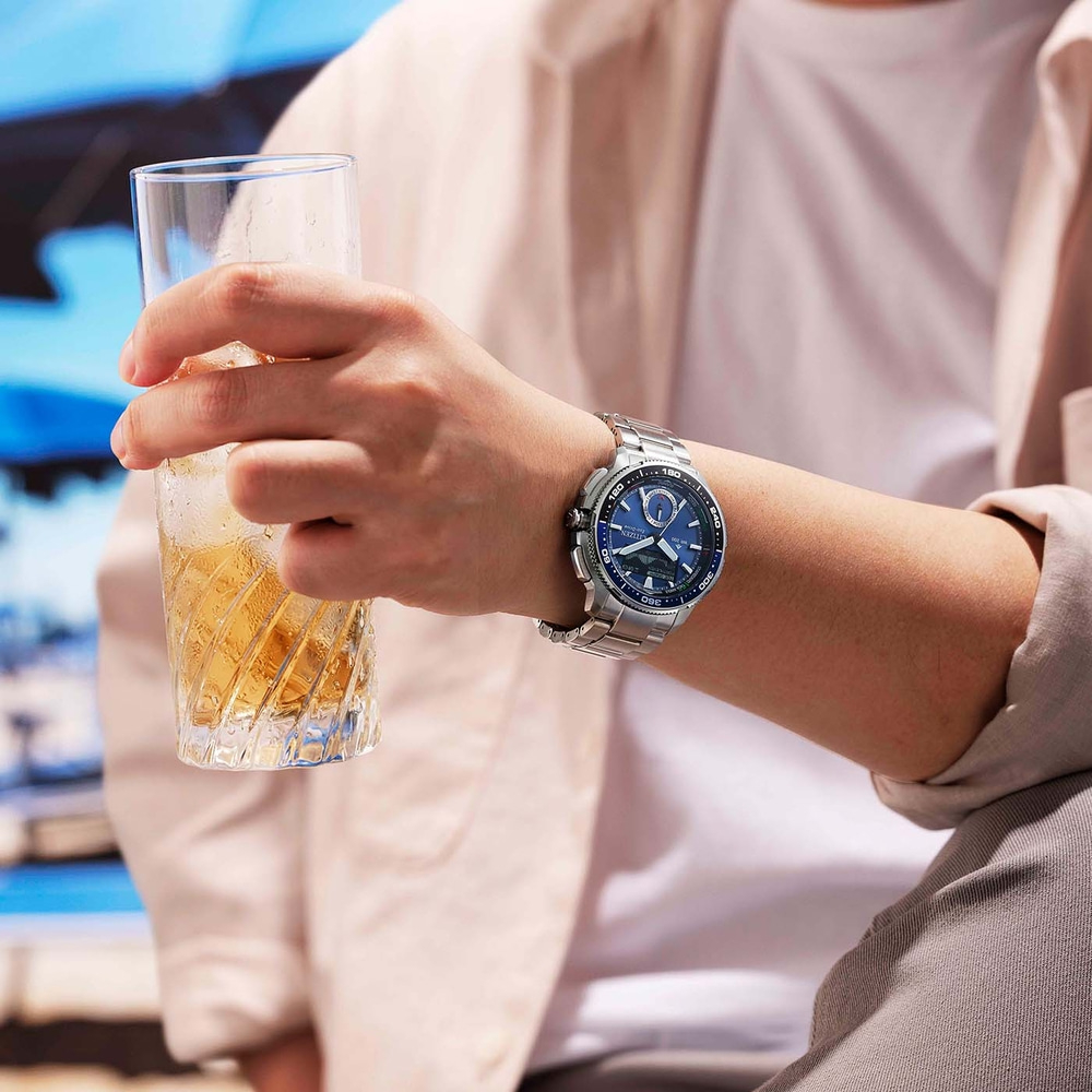 Een persoon houdt een glas met ijzig drankje vast en draagt een zilveren horloge.