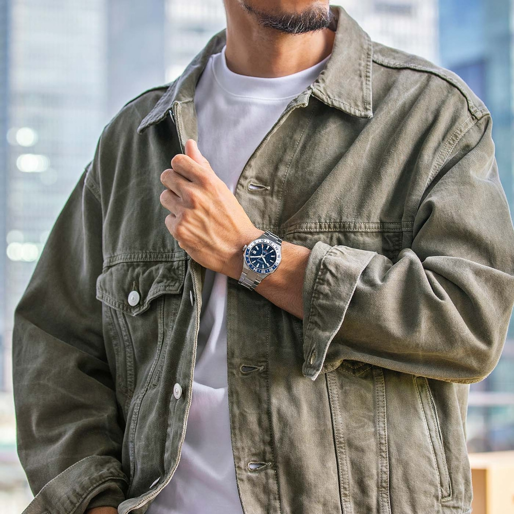 Man met horloge en groene jas, poseert voor een foto.