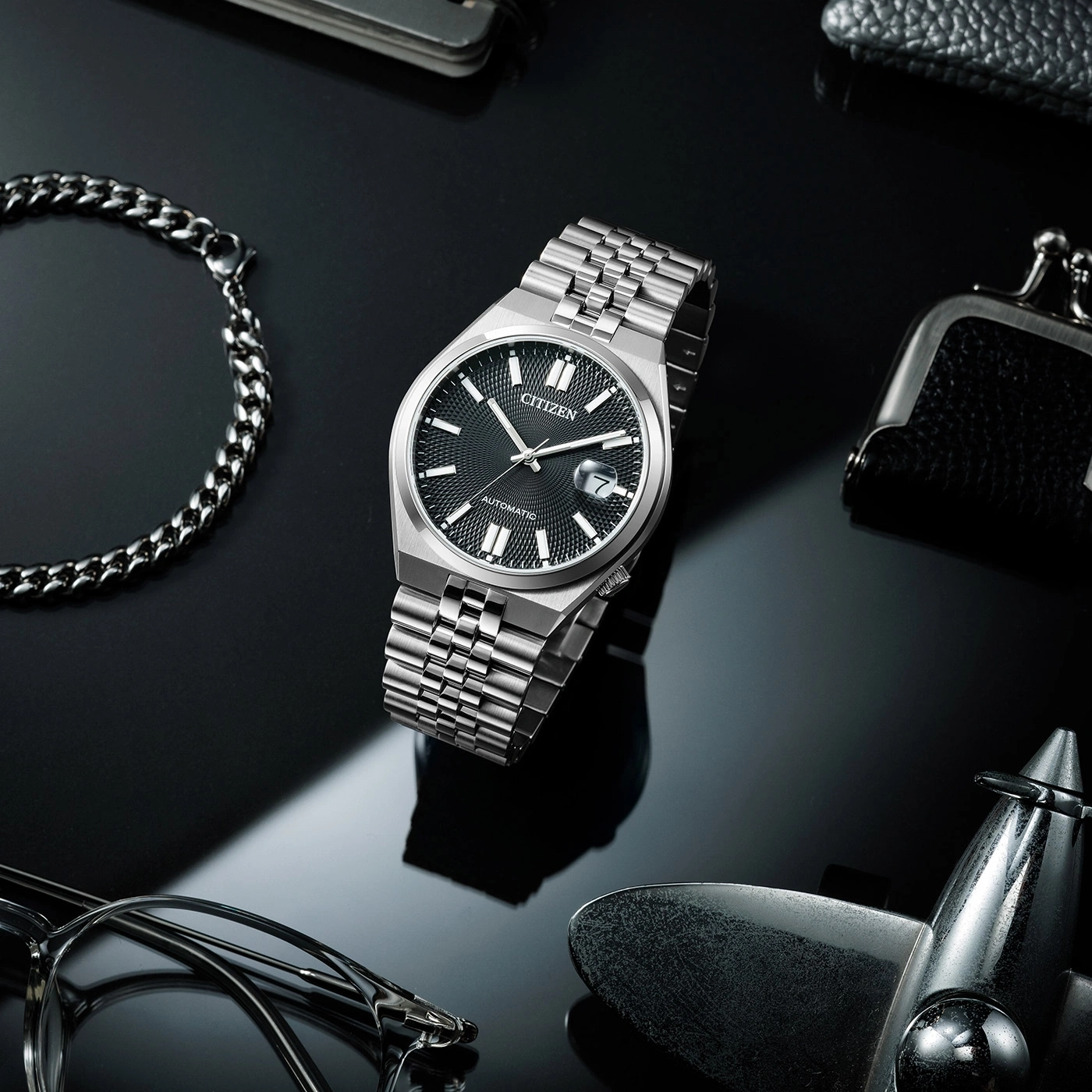 Citizen horloge met armband, bril en accessoires op zwart oppervlak.