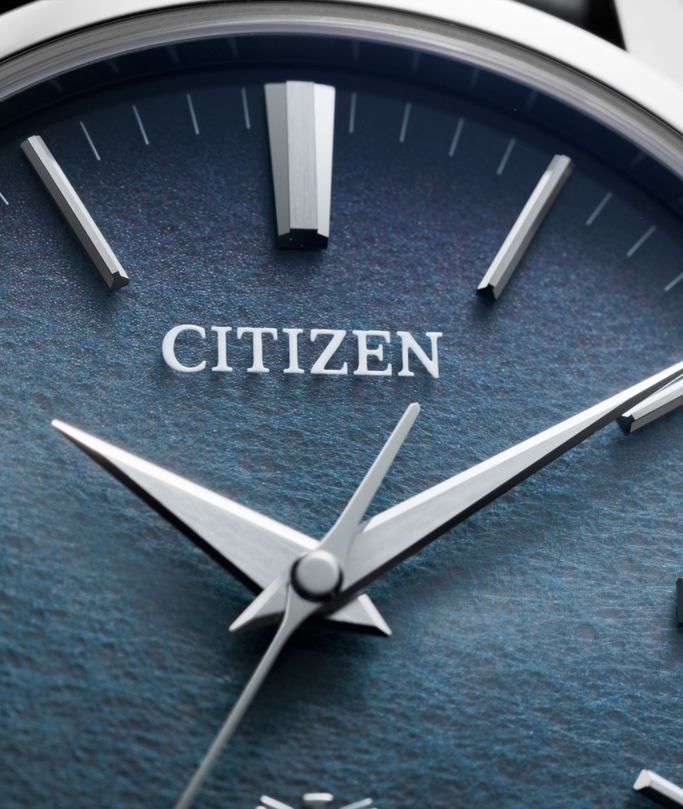 Close-up van een Citizen horlogekast met zilveren wijzers en markeringen op een blauwe, getextureerde wijzerplaat.