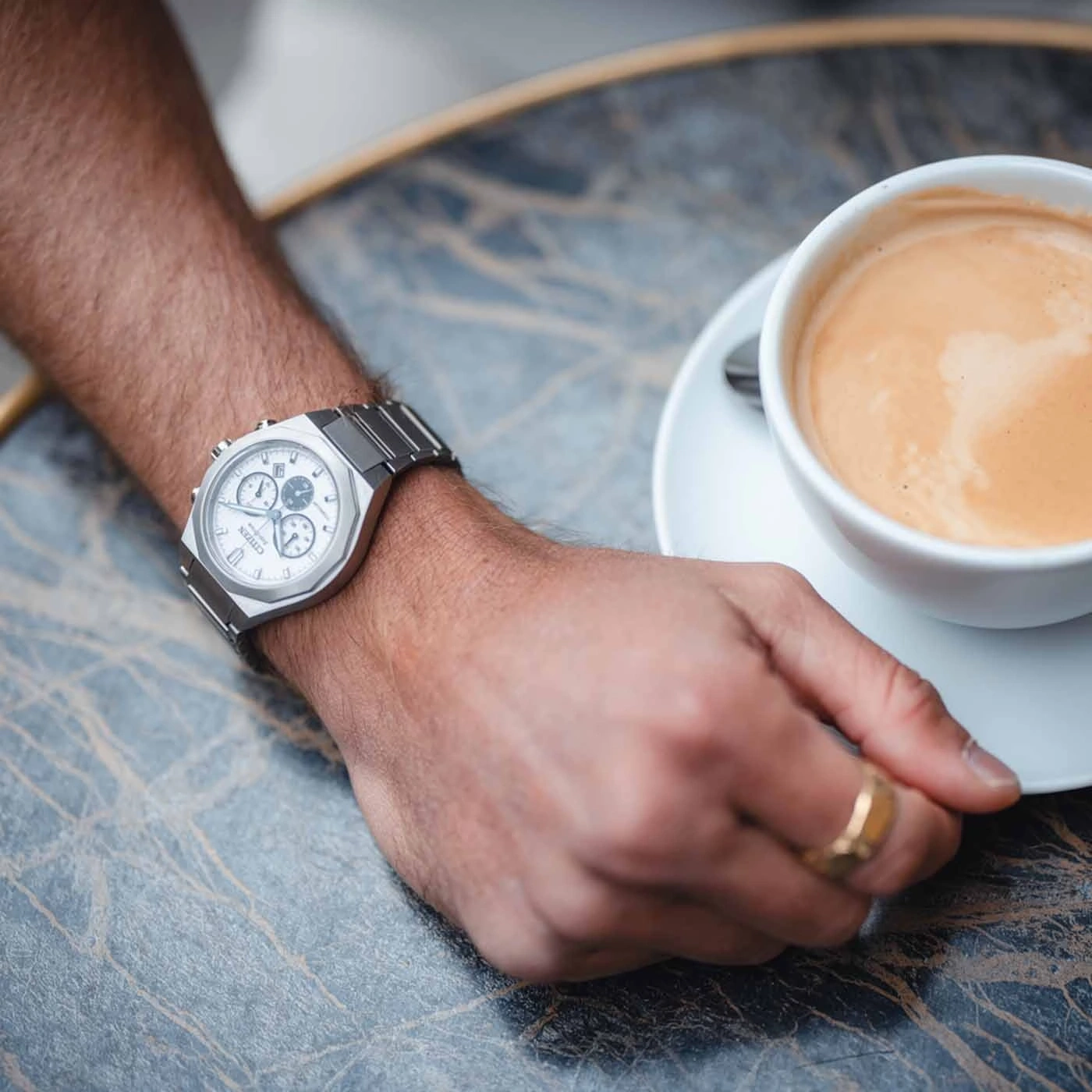 Close-up van een horloge en een koffiekopje op een tafel.