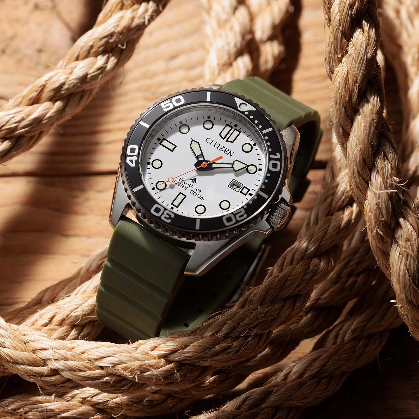 Een Citizen Eco-Drive duikhorloge met witte wijzerplaat en groen bandje, rustend op een houten ondergrond met touw.