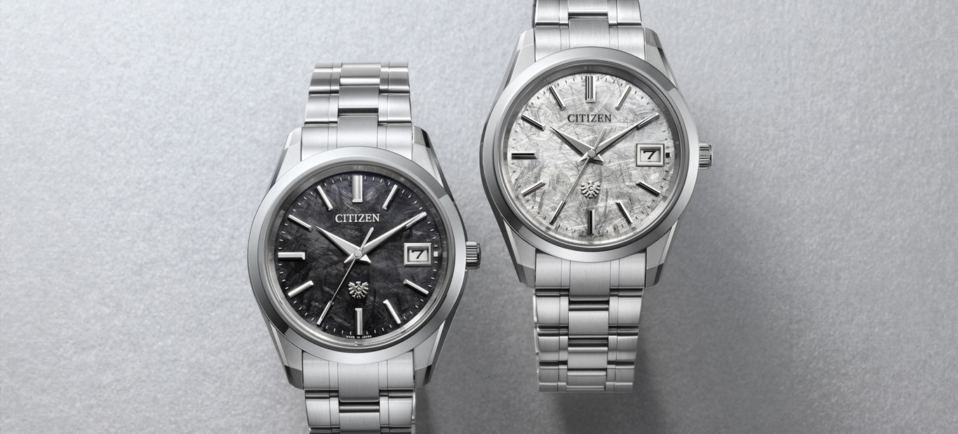 Twee Citizen horloges met zilveren bandjes en getextureerde wijzerplaten op grijze achtergrond.