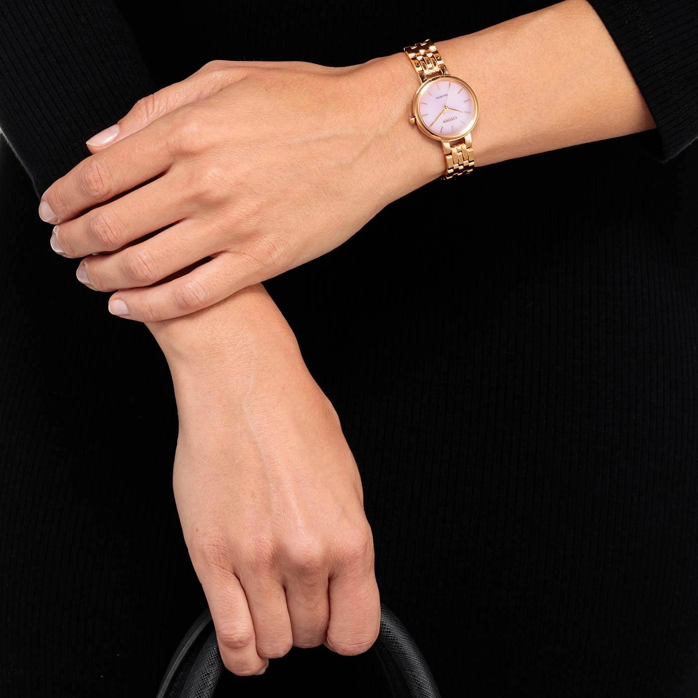 Vrouw met een gouden horloge met roze wijzerplaat, houdt een zwarte tas vast.
