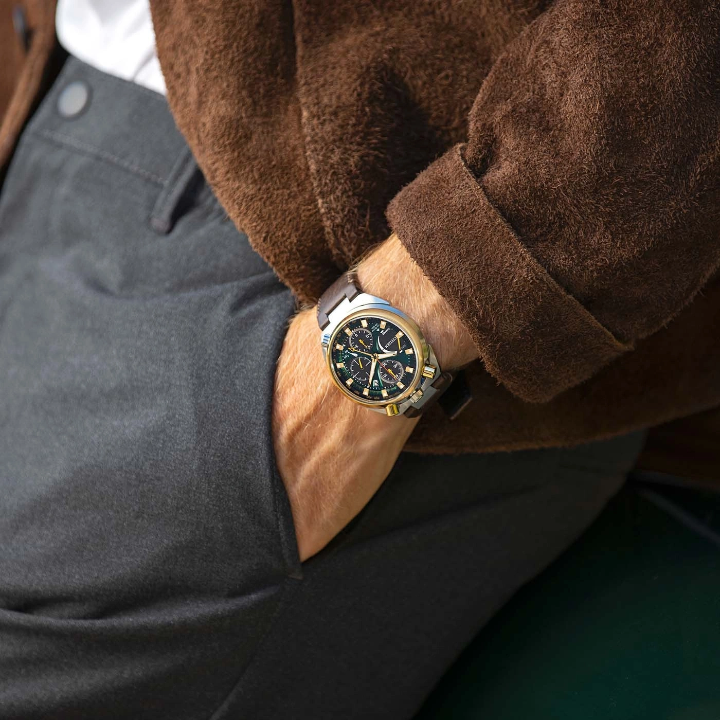Man draagt bruine jas, grijze broek en horloge.