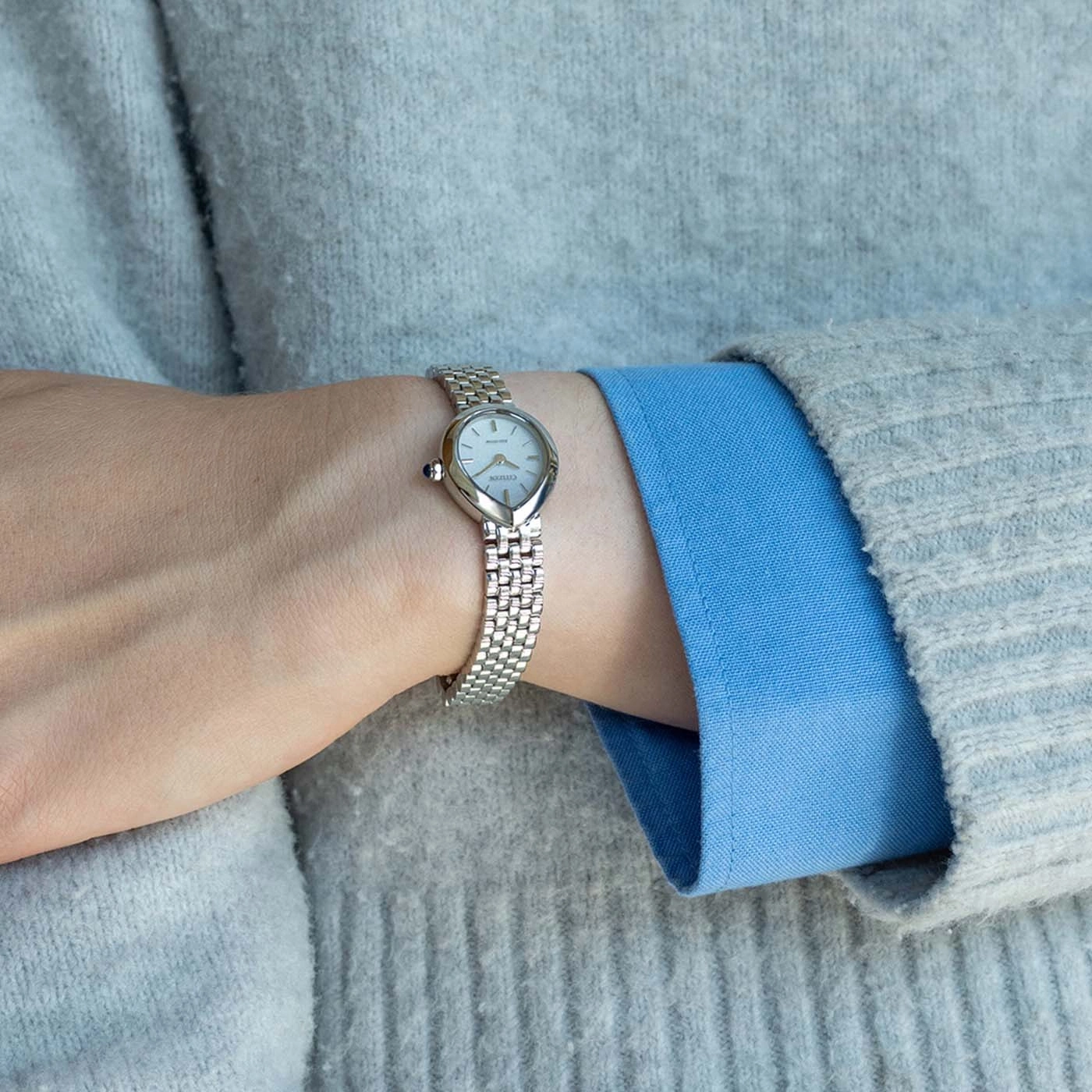 De pols van een vrouw met een zilveren horloge en grijze trui.