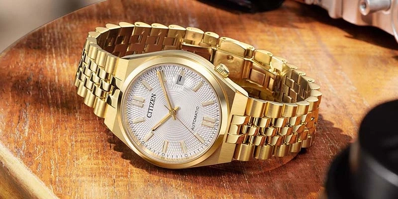 Een gouden Citizen automatische horloge met een getextureerd wijzerplaat op een houten ondergrond.