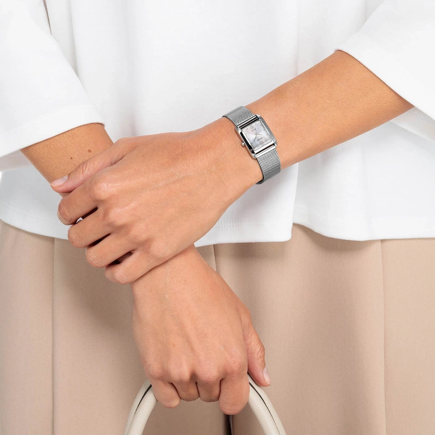 Vrouw met zilveren horloge, witte handtas, beige broek en wit overhemd.