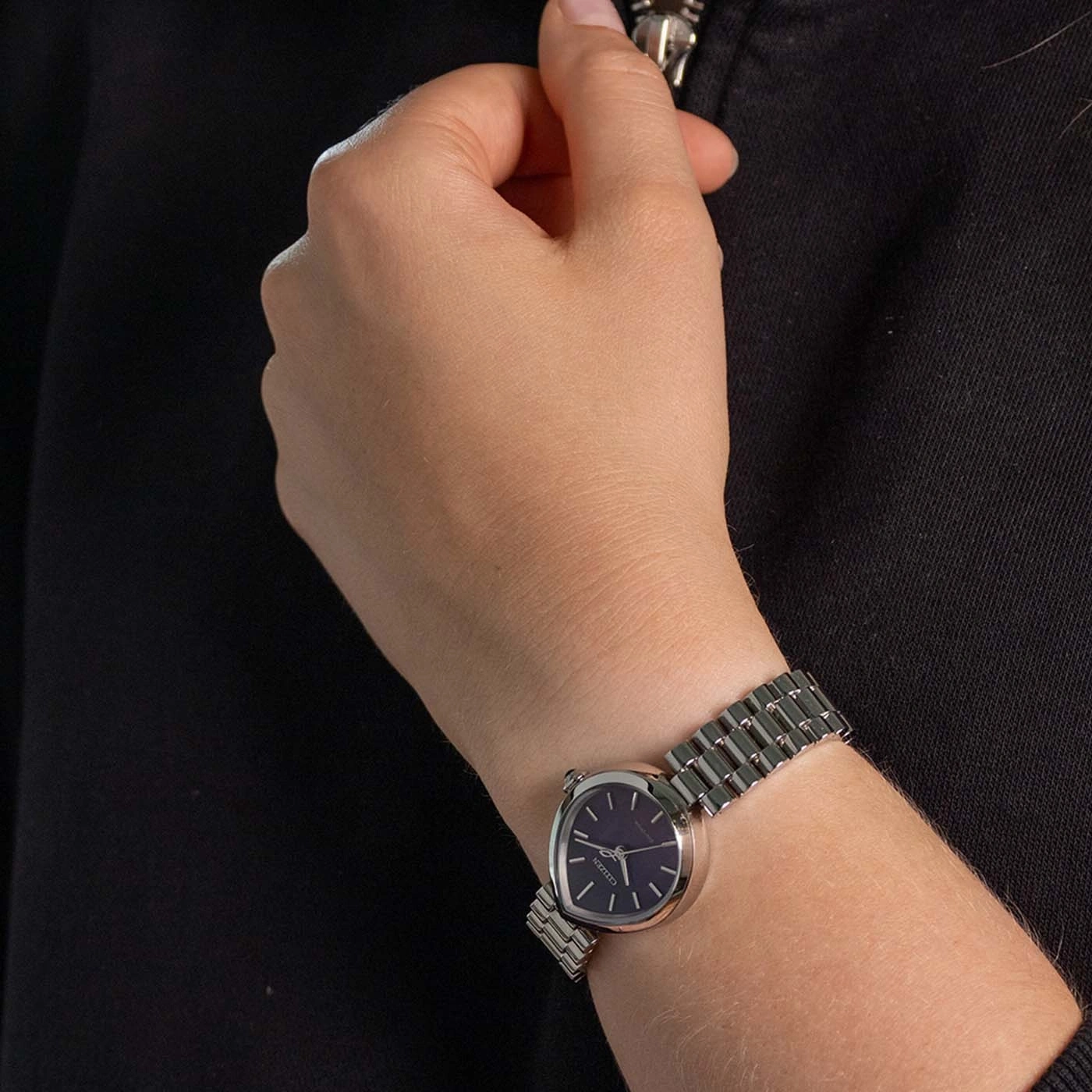 Een vrouwenhand met een zilveren horloge met een donker gezicht.
