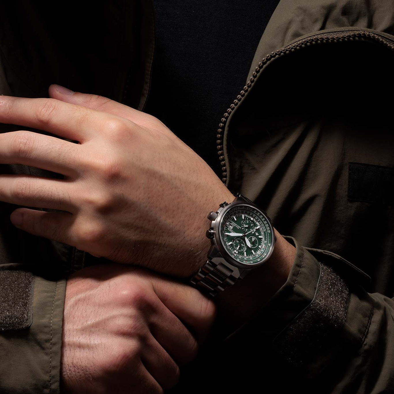 Man met groen horloge, gekruiste handen, donkere jas, close-up.