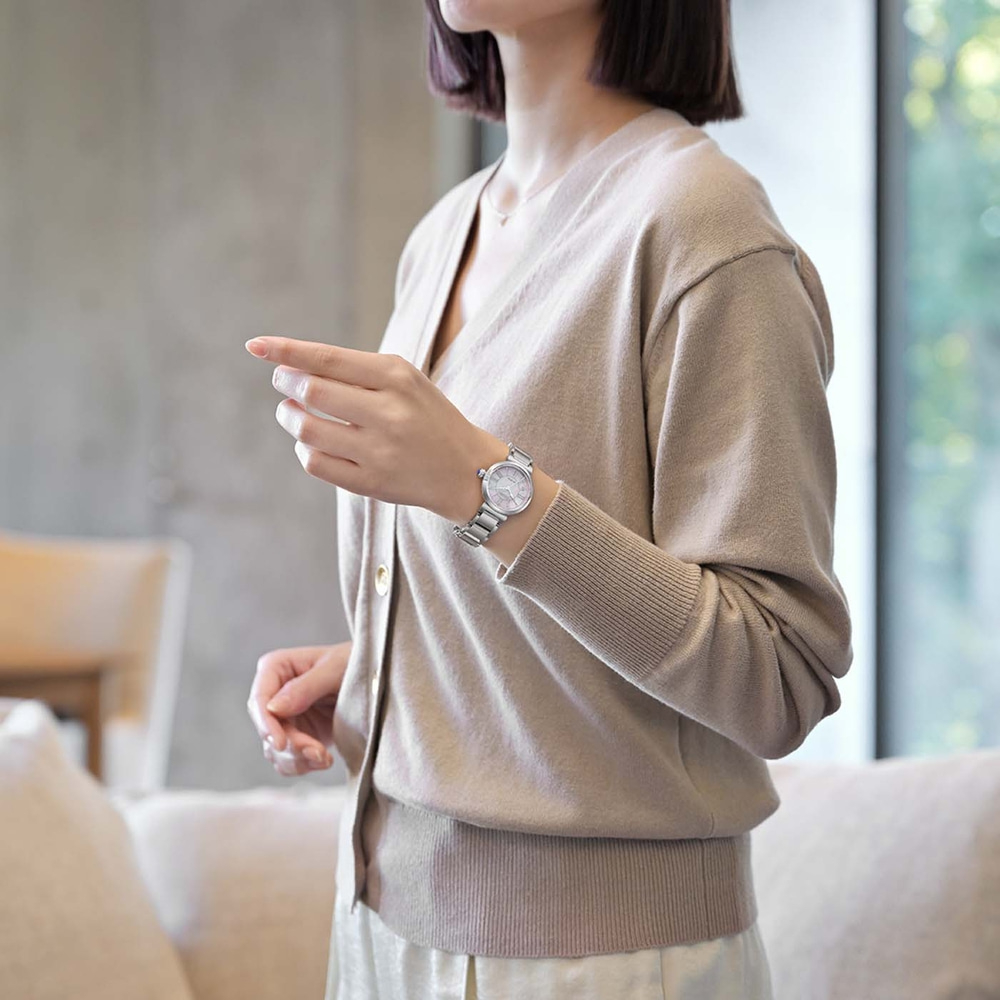 Vrouw draagt een beige vest en een zilveren horloge, wijzend.