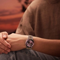 Man draagt een horloge met paarse wijzerplaat en metalen band.