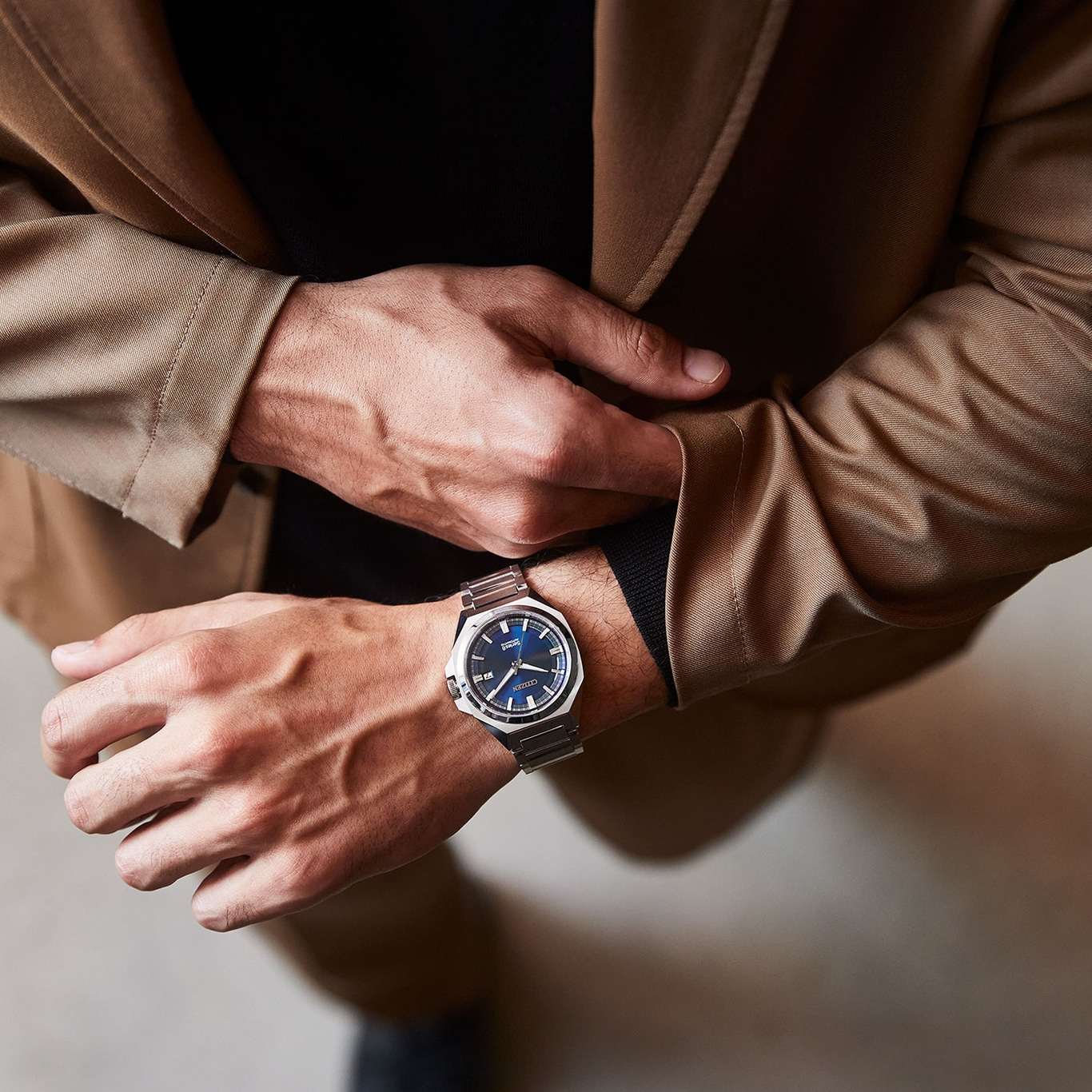 Man met horloge, colbert en zwart overhemd, close-up.