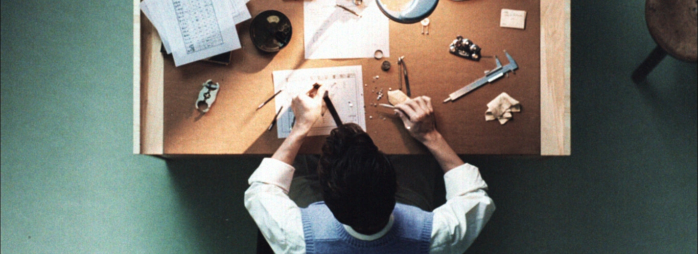 Een persoon die aan een tafel werkt met gereedschap en papieren, bovenaanzicht.