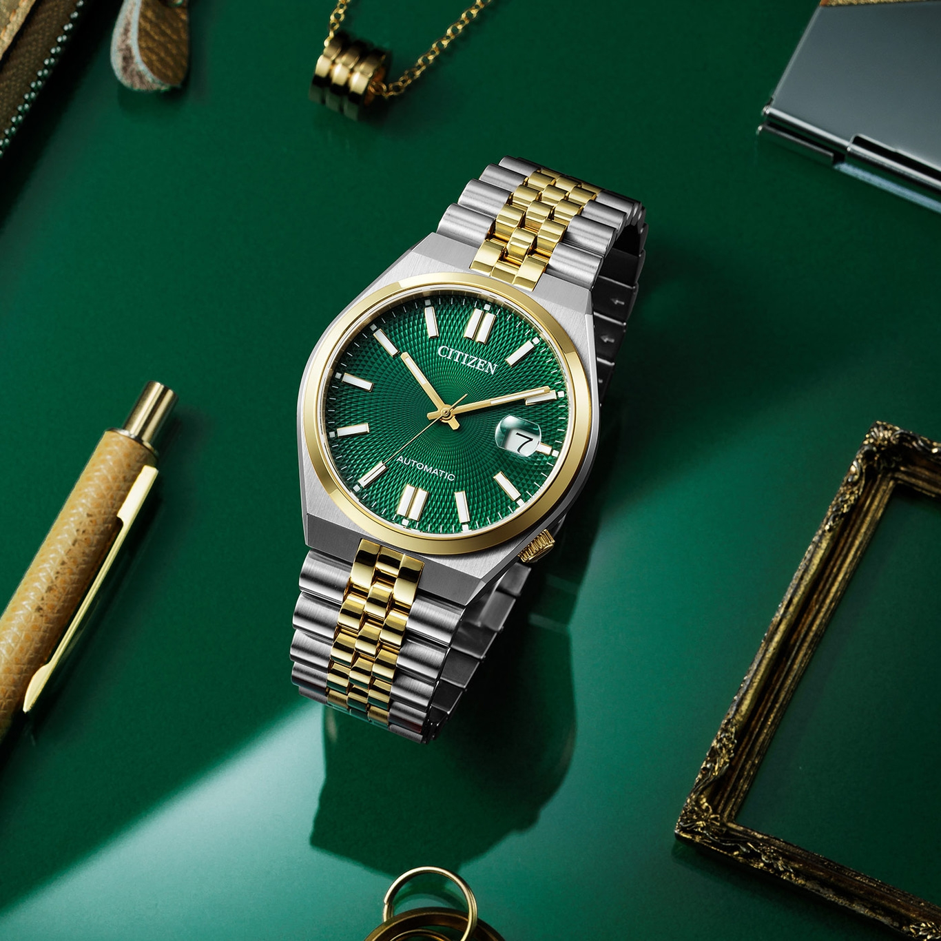 Citizen horloge met groene wijzerplaat en gouden accenten op groene ondergrond.