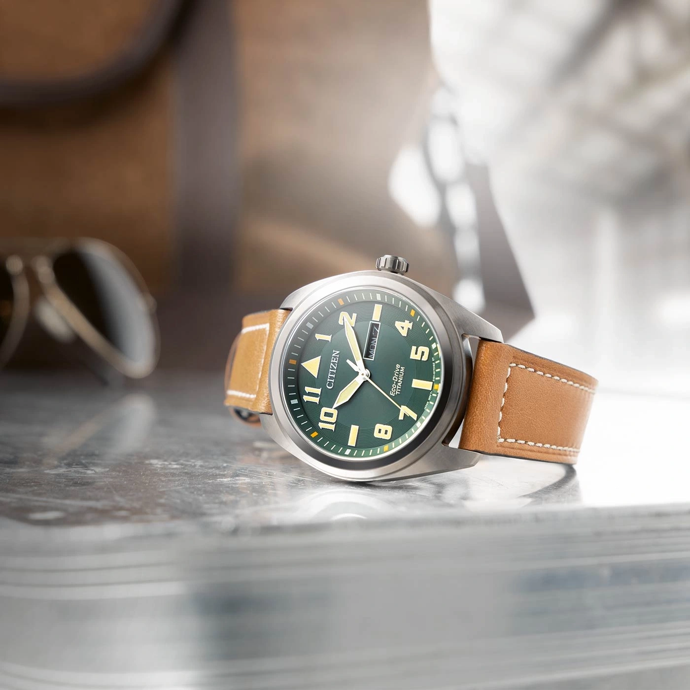 Citizen horloge met groene wijzerplaat en bruine leren band op reflecterend oppervlak.