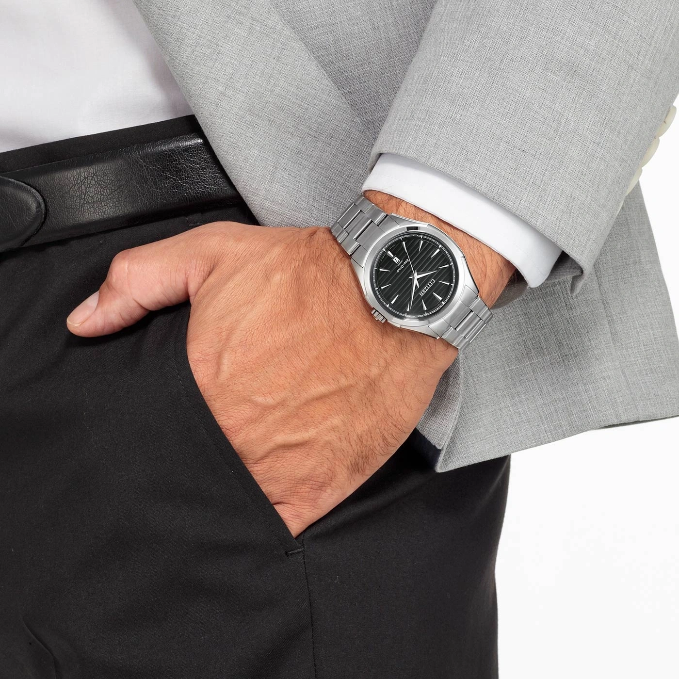 Man met horloge, pak en zwarte broek, hand in de zak.