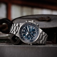 Citizen horloge met blauwe wijzerplaat en metalen band op metalen oppervlak.