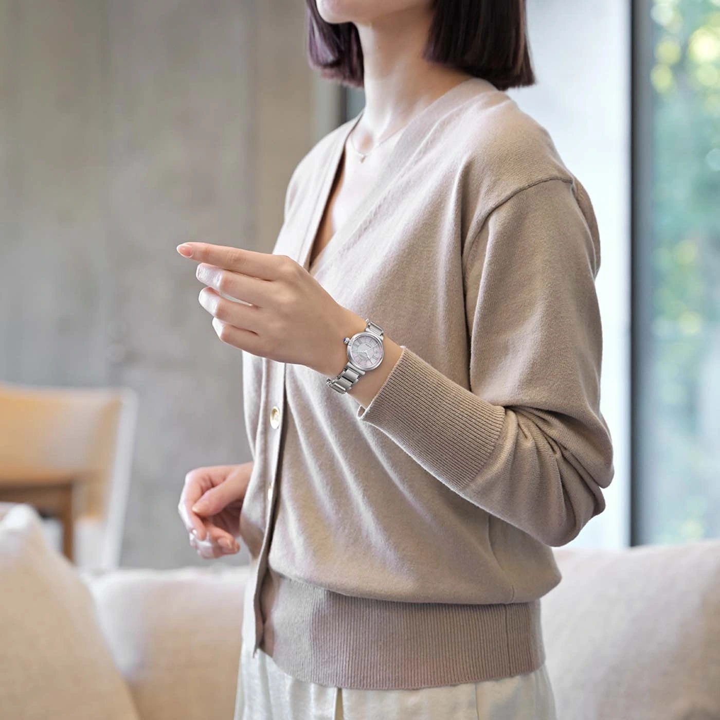 Vrouw draagt een beige vest en een zilveren horloge, wijzend.