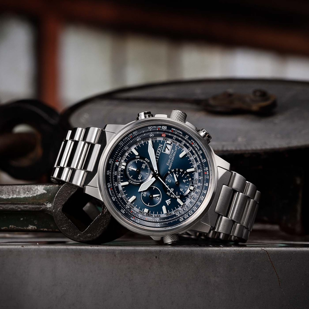 Citizen horloge met blauwe wijzerplaat en metalen band op metalen oppervlak.