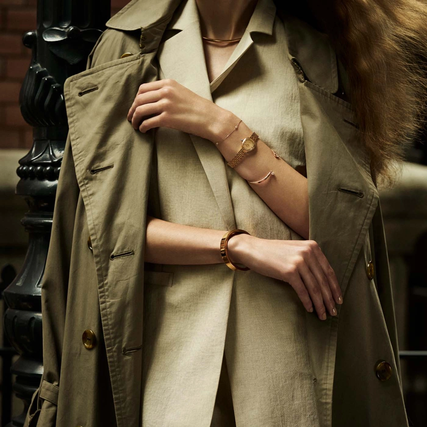 Vrouw draagt een trenchcoat en sieraden, close-up van armen.