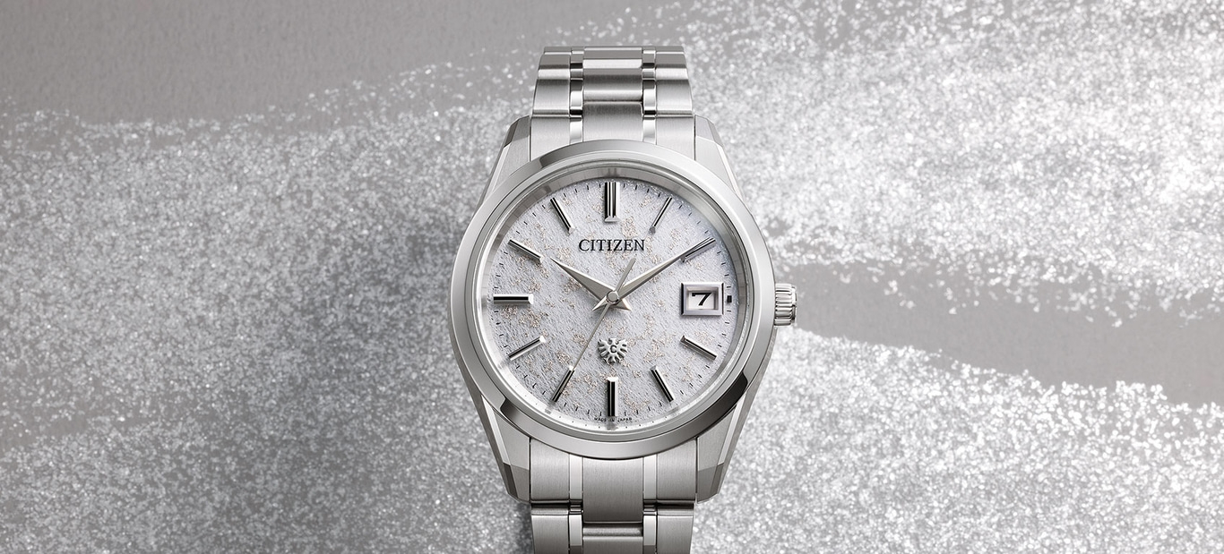 Citizen horloge met zilveren band en witte wijzerplaat op zilveren achtergrond.