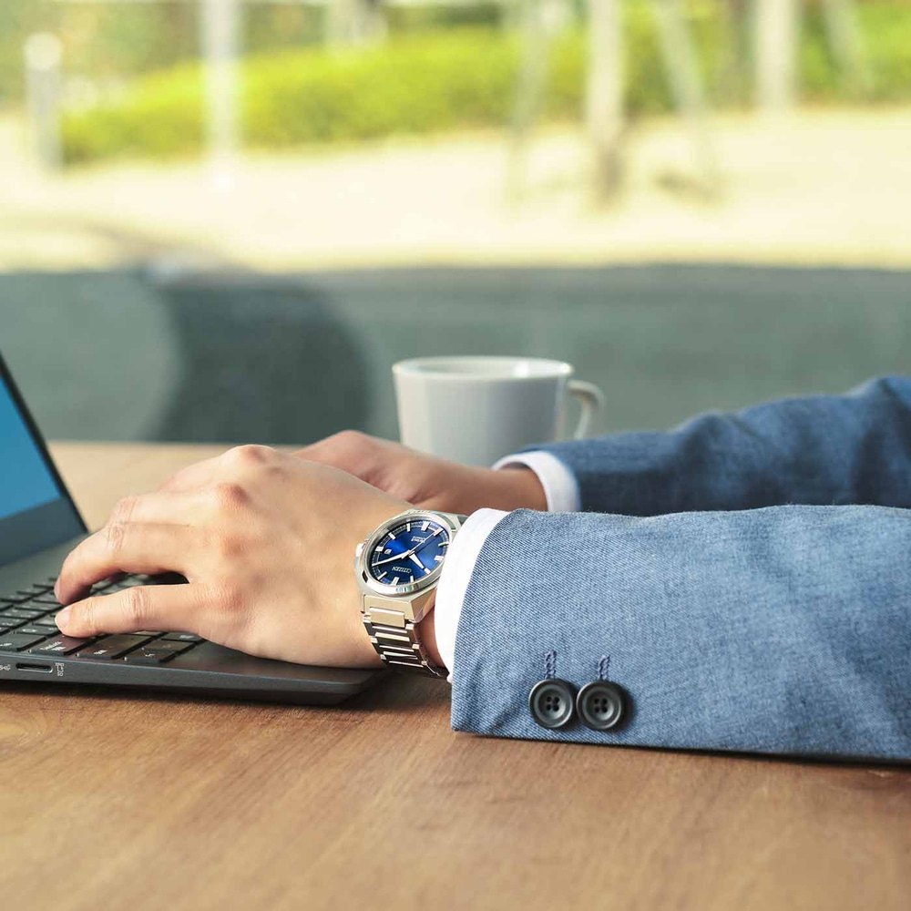 Man met horloge, typt op laptop, met een kopje koffie op tafel.