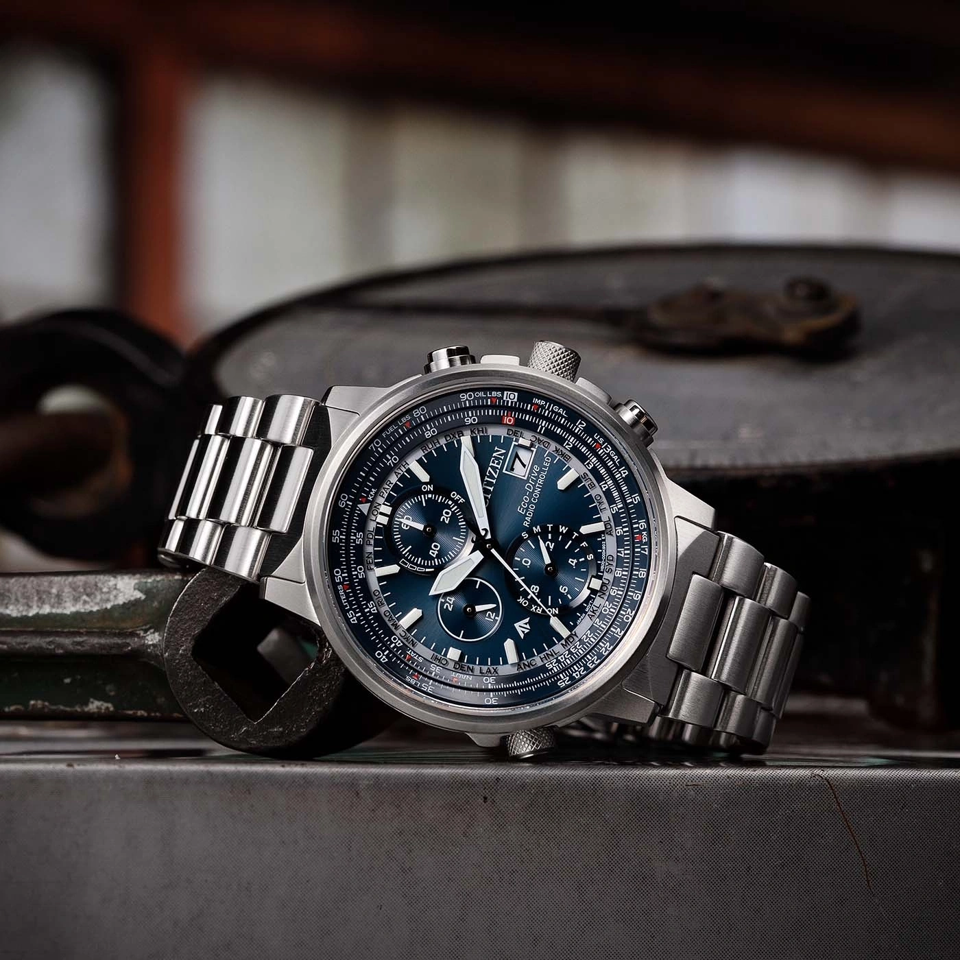 Citizen horloge met blauwe wijzerplaat en metalen band op metalen oppervlak.