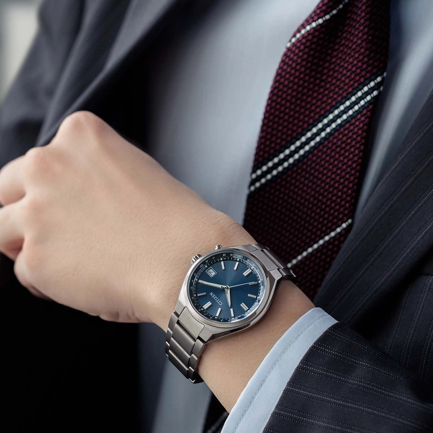 Een man in een pak draagt een blauw Citizen horloge om zijn pols.