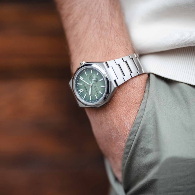 Een persoon die een Citizen-horloge draagt met een groene wijzerplaat en zilveren armband.