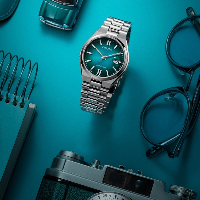 Citizen horloge, bril, camera, speelgoedauto en notitieboek op blauwe ondergrond.