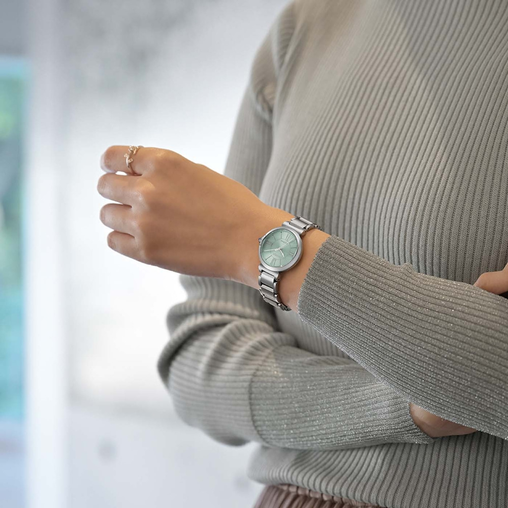 Een vrouw met een zilveren horloge en een grijze trui.