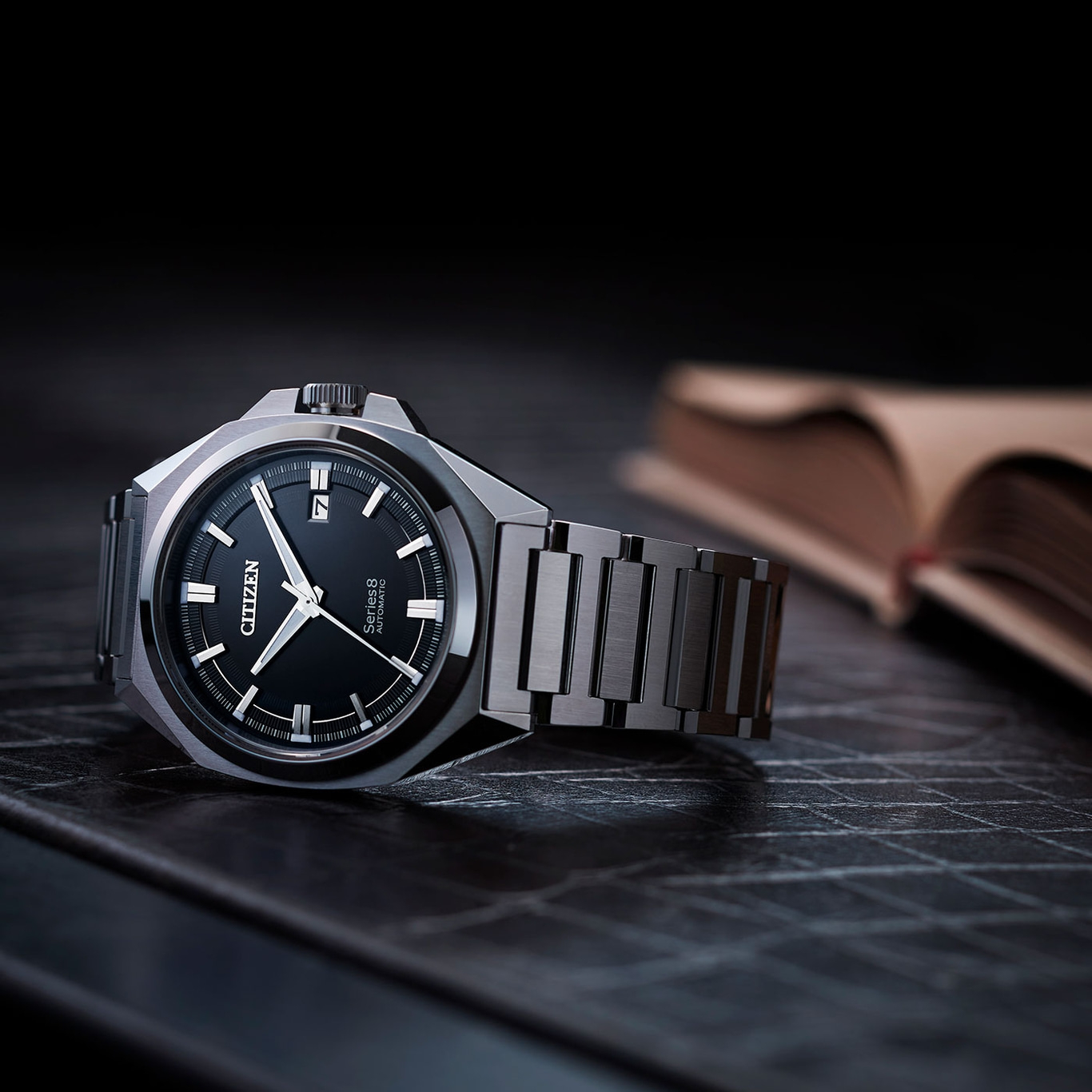 Citizen horloge met zwarte wijzerplaat en metalen band op donkere ondergrond.