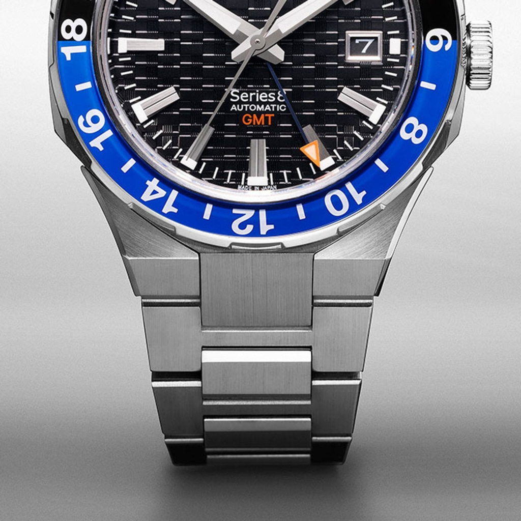 Close-up van een zilveren horloge met een blauwe bezel en zwarte wijzerplaat.