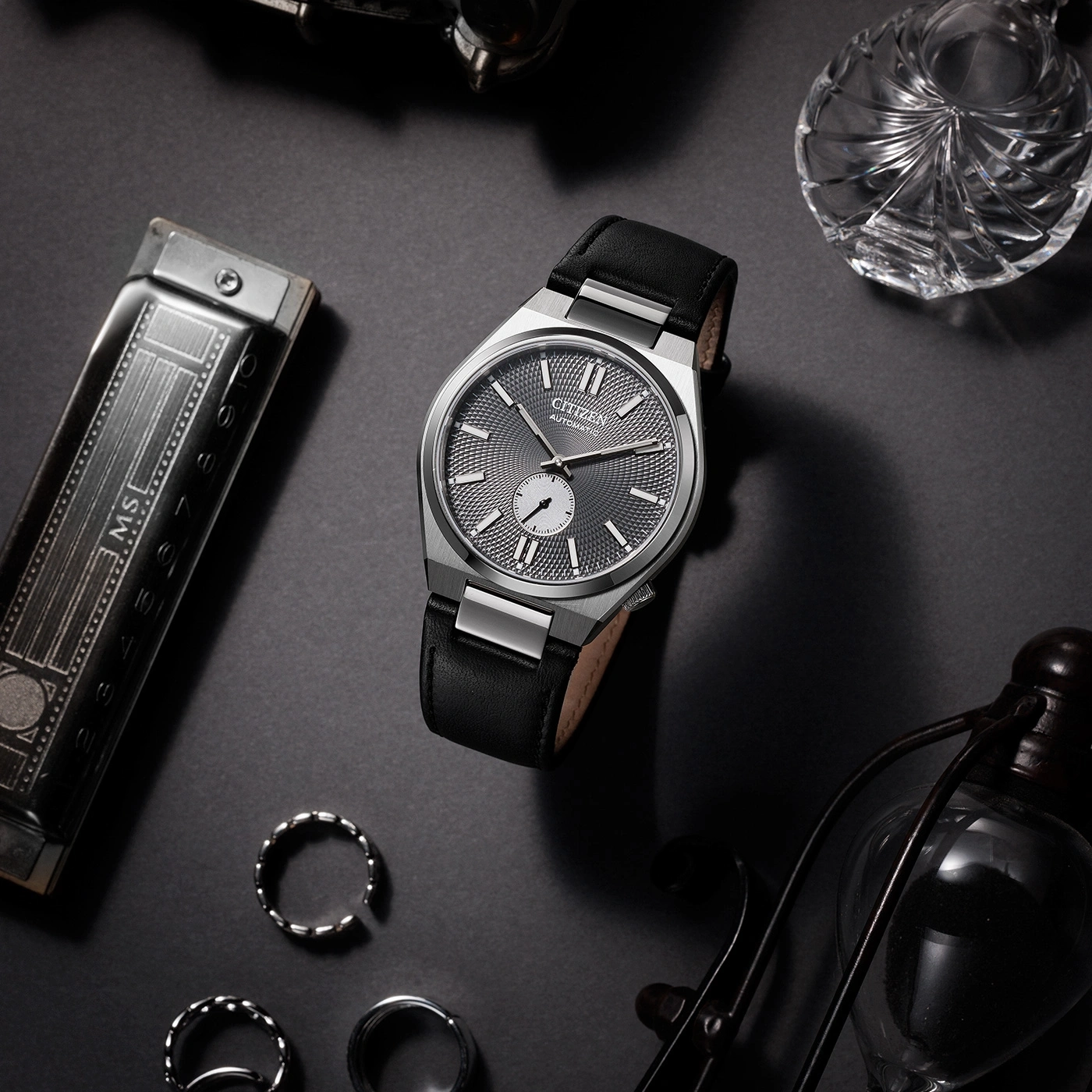 Citizen horloge met zwarte leren band en accessoires op een donkere ondergrond.
