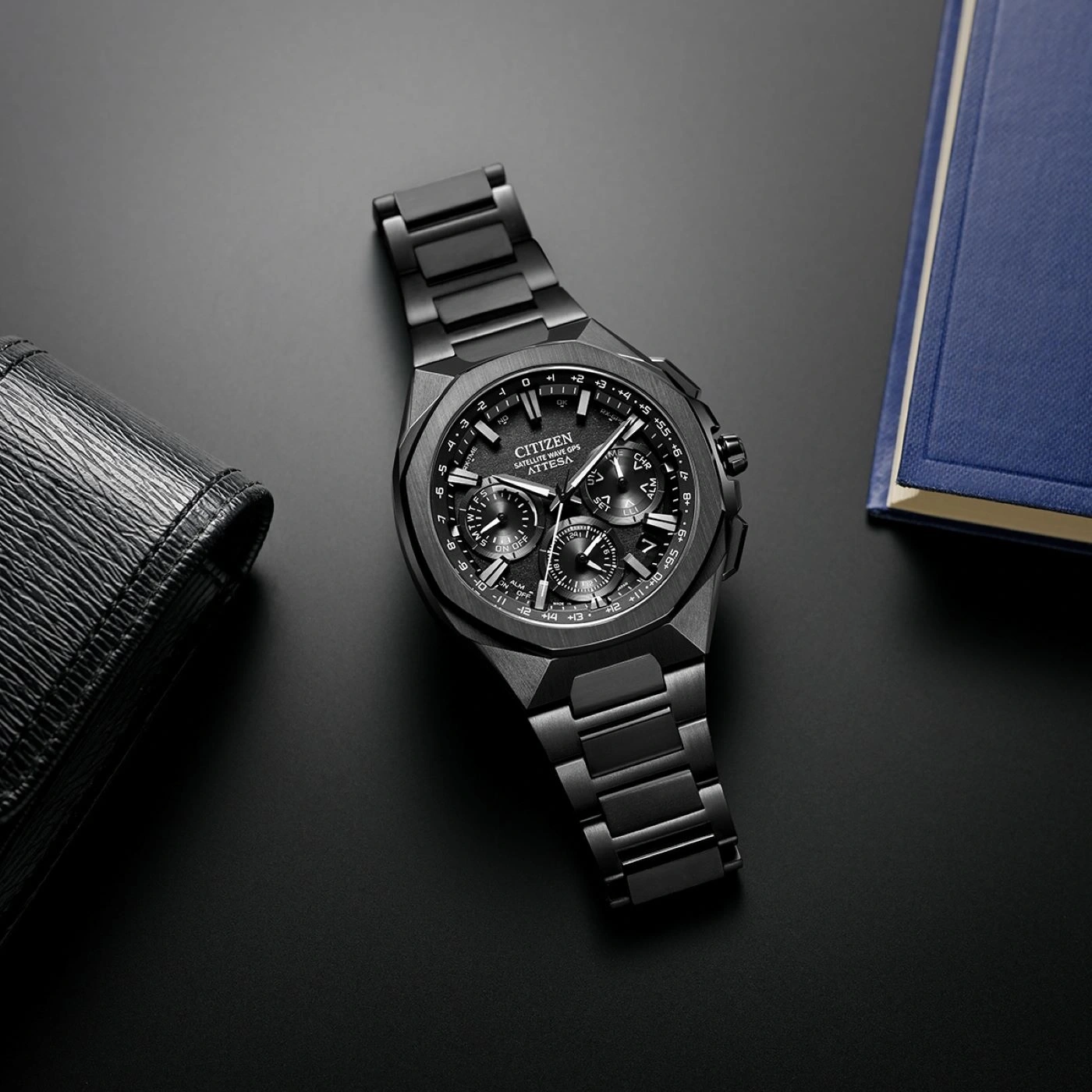 Zwart Citizen horloge op een zwart oppervlak met een portemonnee en een boek.