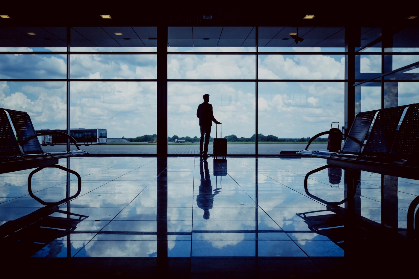 Silhouet van een persoon met bagage op een luchthaven, uit het raam kijkend.