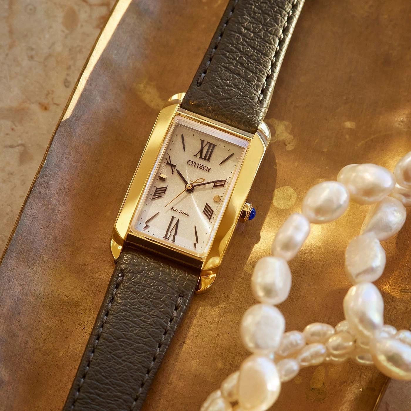 Citizen horloge met gouden kast en leren band, naast parels.