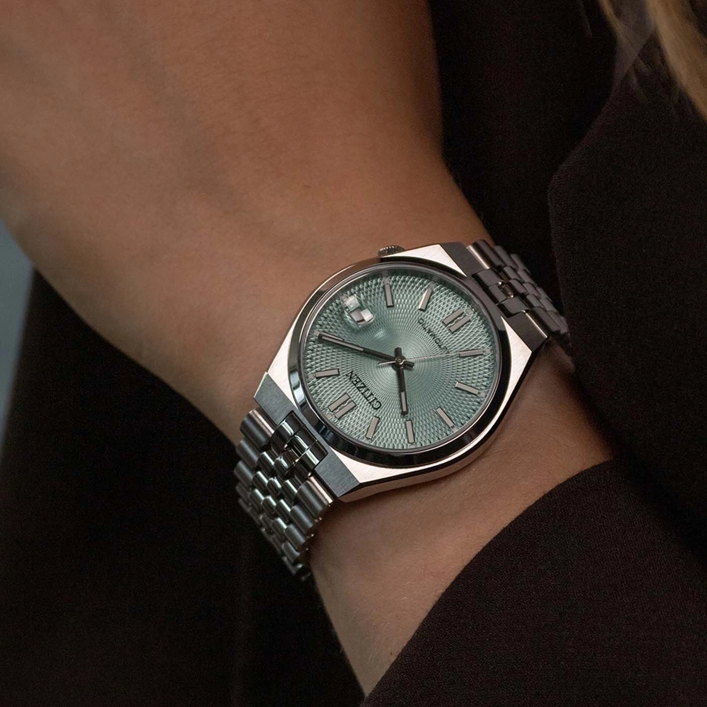 Een persoon draagt een Citizen horloge met een groen wijzerplaat om de pols.