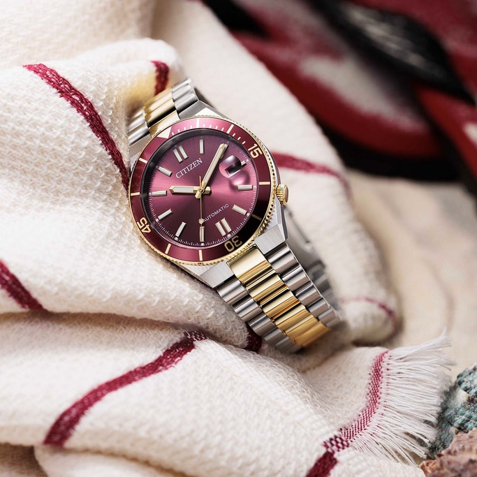 Close-up van een Citizen automatisch horloge met een rood wijzerplaat en gouden accenten.
