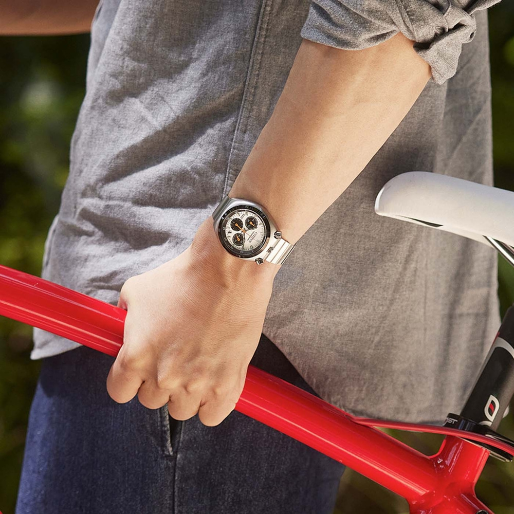 Persoon in grijs shirt houdt rode fietsframe vast, draagt een horloge.