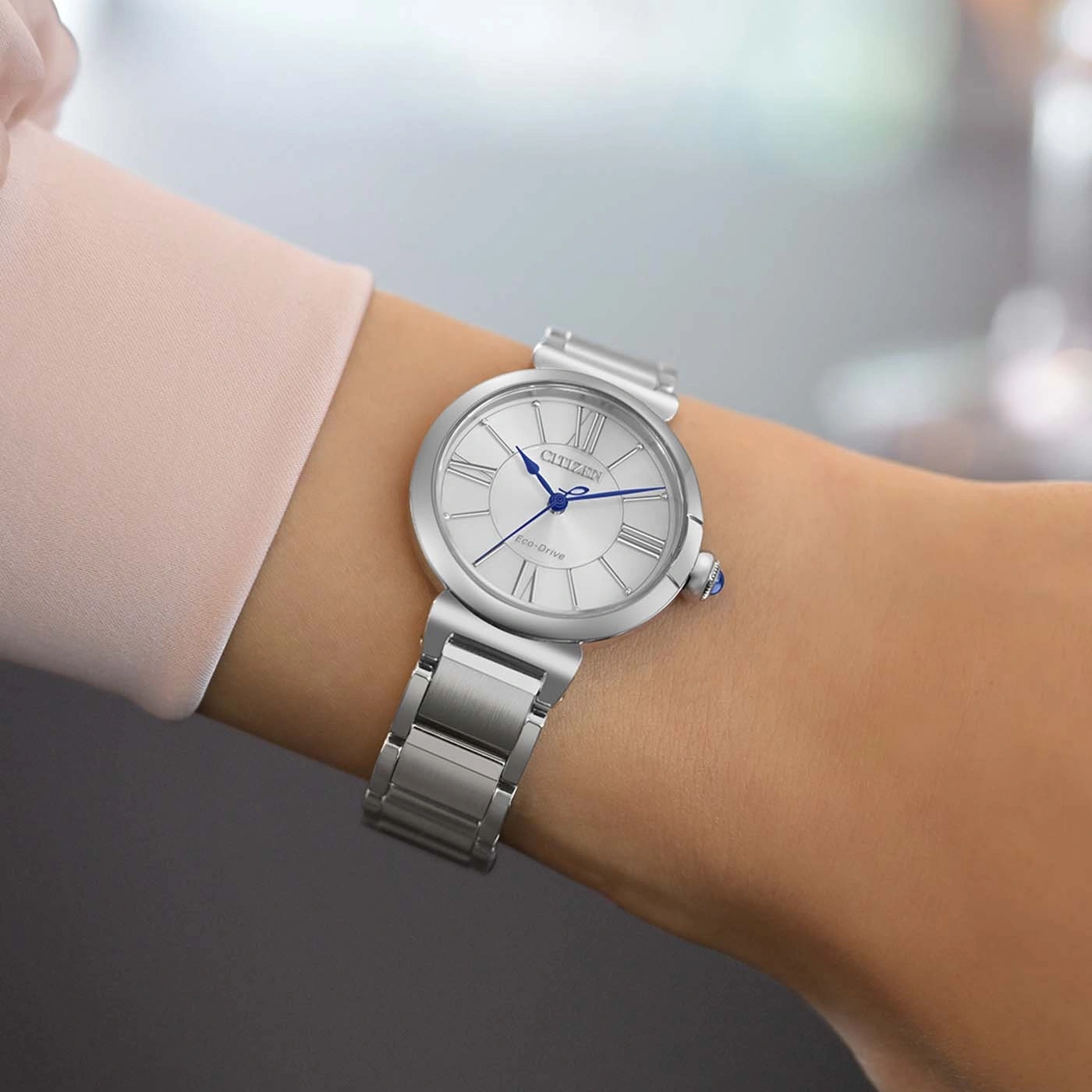 Een vrouw draagt een zilveren Citizen Eco-Drive horloge met Romeinse cijfers.