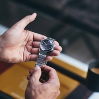 Close-up van een persoon die een Citizen-horloge met een zwarte wijzerplaat vasthoudt.