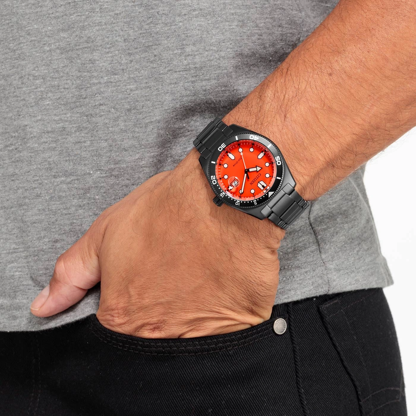 Man met een zwart horloge met een oranje wijzerplaat, grijs shirt en zwarte broek.