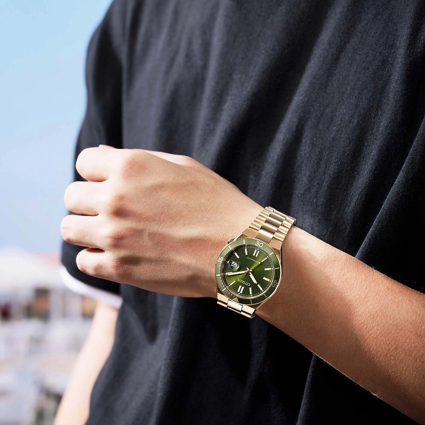 Man draagt een gouden Citizen horloge met groene wijzerplaat.