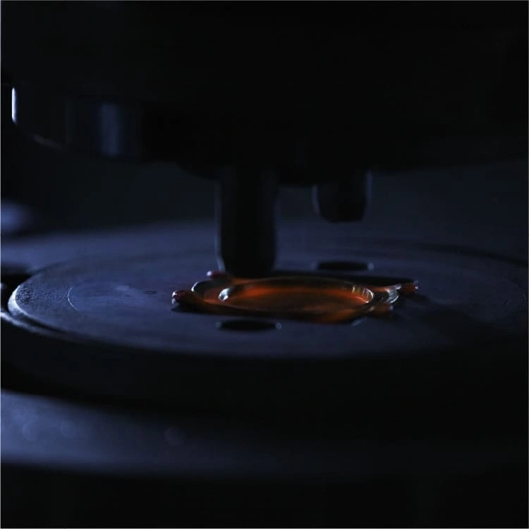 Close-up van een donkere machine met een druppel oranje vloeistof op een plaat.