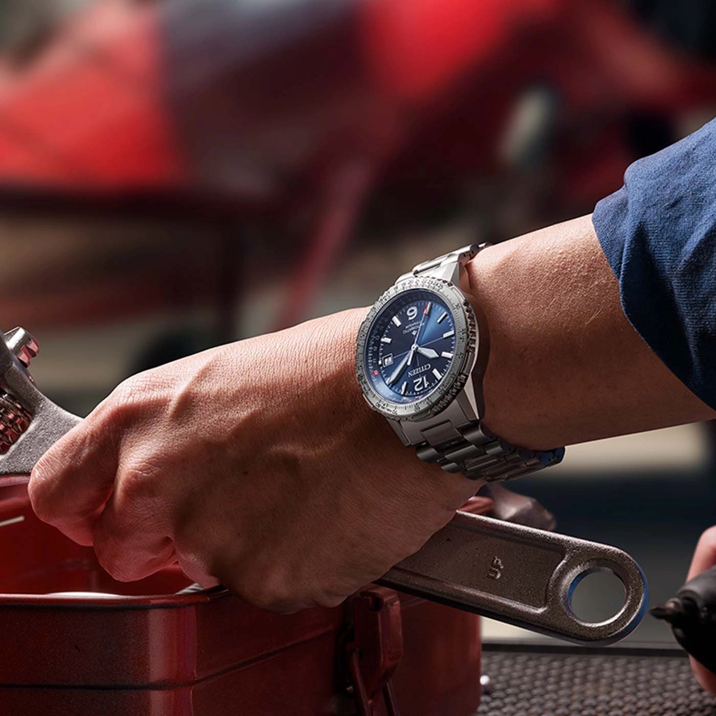 Close-up van een persoon die een horloge draagt en een moersleutel vasthoudt, werkend aan een auto.